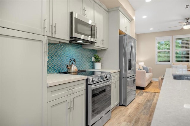 kitchen featuring appliances with stainless steel finishes, white cabinetry, decorative backsplash, ceiling fan, and light hardwood / wood-style floors