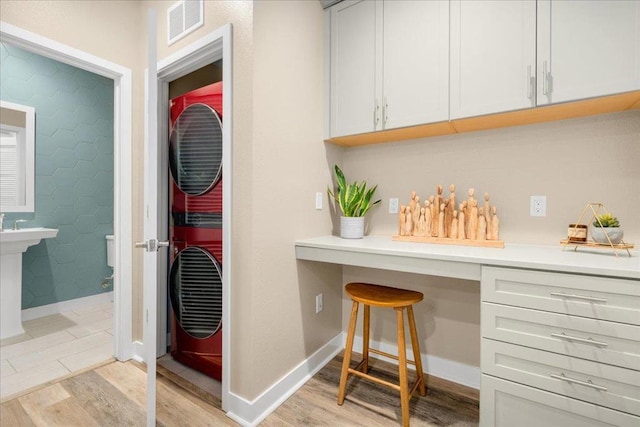 interior space featuring white cabinetry, stacked washer and dryer, built in desk, and light hardwood / wood-style floors