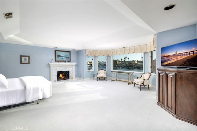 carpeted bedroom featuring a high end fireplace and a raised ceiling