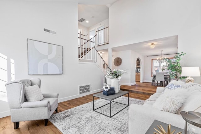 living room featuring a towering ceiling, wood-type flooring, and a notable chandelier