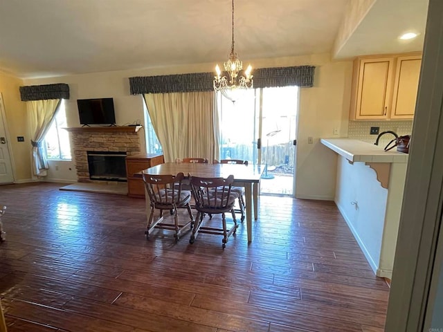 dining area featuring an inviting chandelier, a stone fireplace, and dark hardwood / wood-style floors