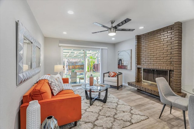 living room featuring a brick fireplace, ceiling fan, and light wood-type flooring