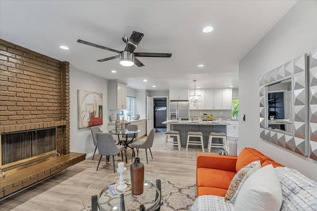 living room with a brick fireplace, light wood-type flooring, and ceiling fan