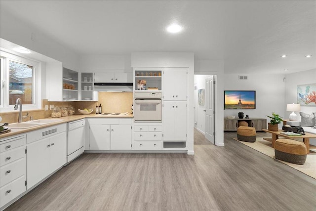 kitchen featuring sink, light wood-type flooring, backsplash, white cabinets, and white appliances