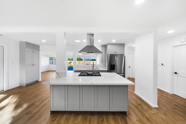 kitchen featuring island range hood, gray cabinetry, stainless steel fridge, kitchen peninsula, and light stone countertops