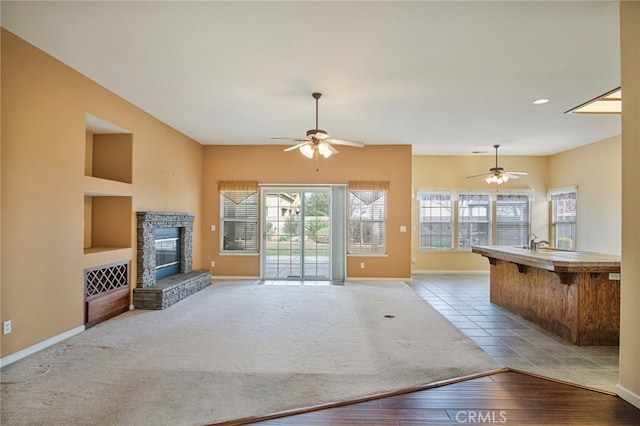 unfurnished living room featuring a stone fireplace, light carpet, and ceiling fan