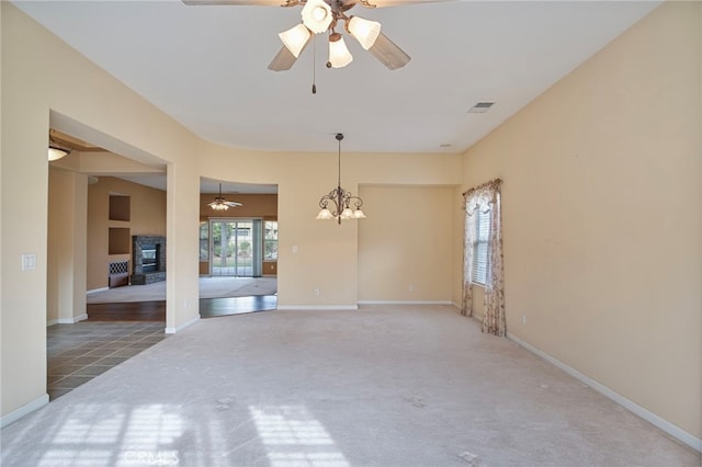 carpeted empty room with a fireplace and ceiling fan with notable chandelier