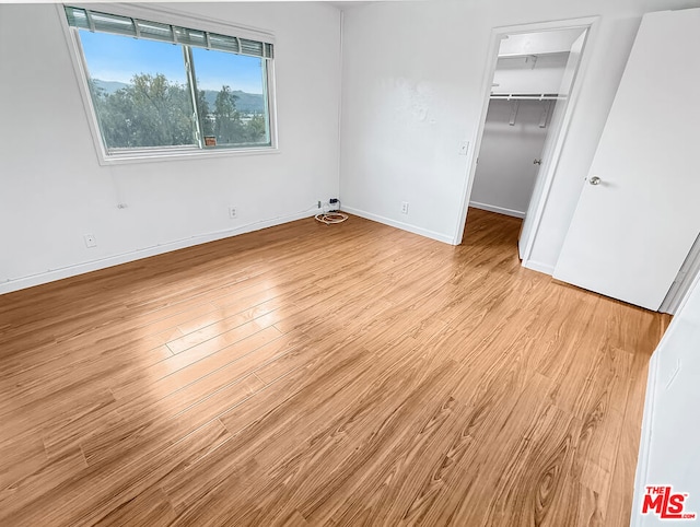 unfurnished bedroom with a spacious closet, a closet, and light wood-type flooring