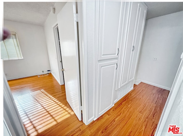 corridor with a textured ceiling and light wood-type flooring