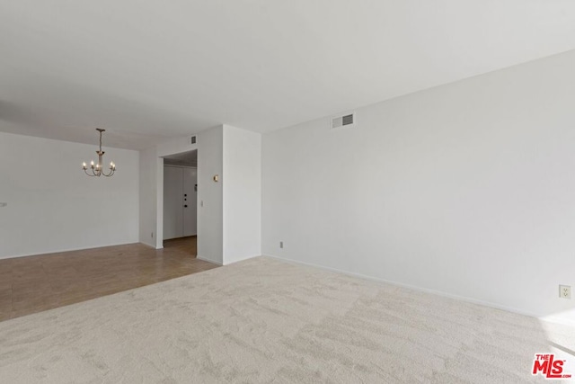 carpeted empty room with an inviting chandelier