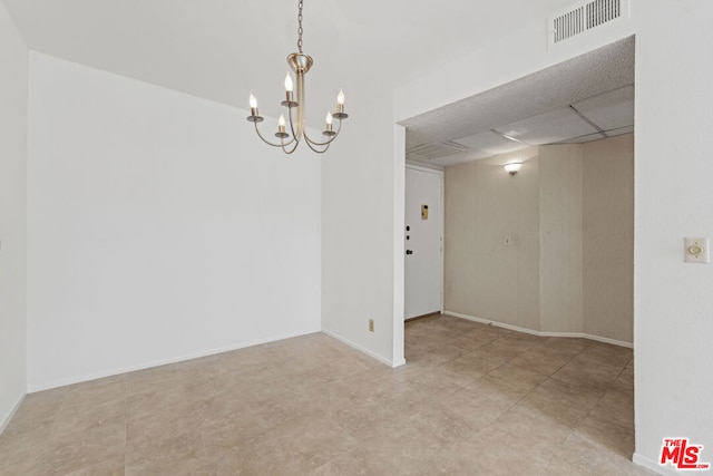 spare room featuring a drop ceiling and an inviting chandelier