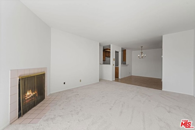 unfurnished living room with a tiled fireplace, light colored carpet, and an inviting chandelier