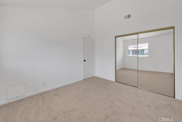 unfurnished bedroom with light colored carpet, a closet, and a towering ceiling