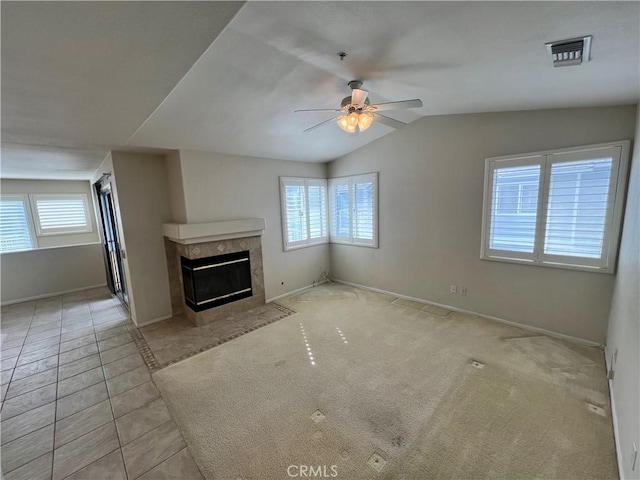 unfurnished living room with ceiling fan, lofted ceiling, a tiled fireplace, and light carpet