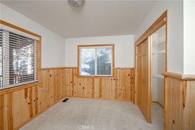 empty room featuring a healthy amount of sunlight, light carpet, and wood walls