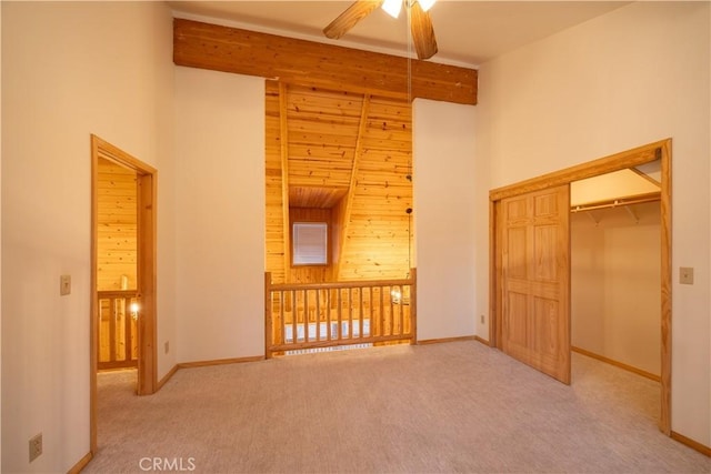 unfurnished bedroom with wood walls, carpet flooring, beam ceiling, and a high ceiling