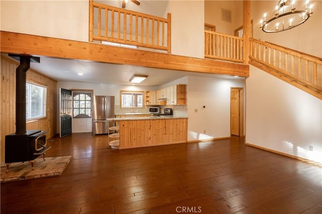 kitchen with appliances with stainless steel finishes, dark hardwood / wood-style flooring, light brown cabinets, and a wood stove