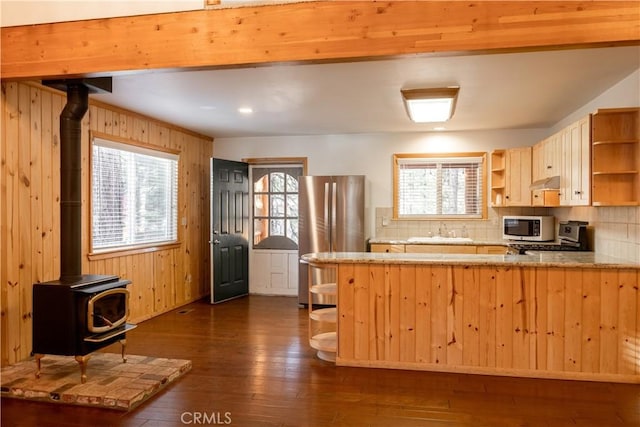 kitchen featuring sink, dark wood-type flooring, a wood stove, stainless steel refrigerator, and wood walls