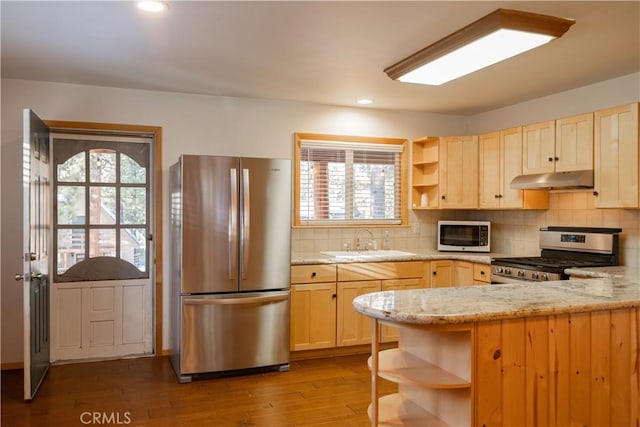 kitchen with appliances with stainless steel finishes, sink, kitchen peninsula, light stone countertops, and light hardwood / wood-style flooring