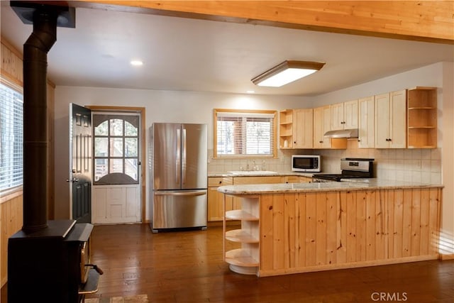 kitchen with a wood stove, stainless steel appliances, dark hardwood / wood-style floors, kitchen peninsula, and light brown cabinets