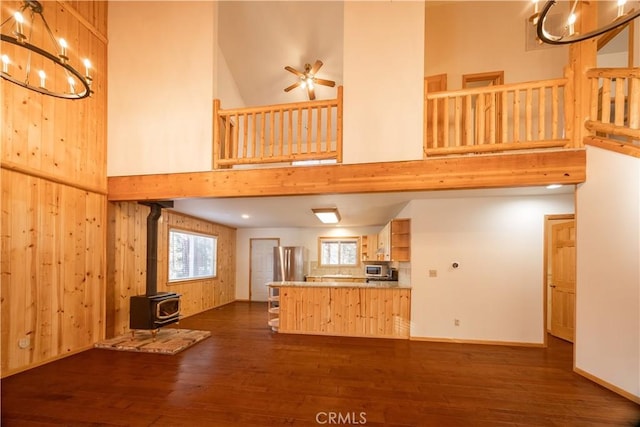 unfurnished living room with ceiling fan, wooden walls, a high ceiling, dark hardwood / wood-style flooring, and a wood stove