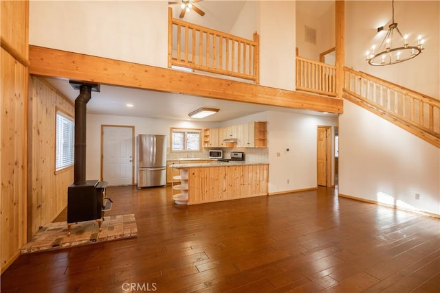 unfurnished living room featuring ceiling fan with notable chandelier, a wood stove, dark wood-type flooring, and wood walls