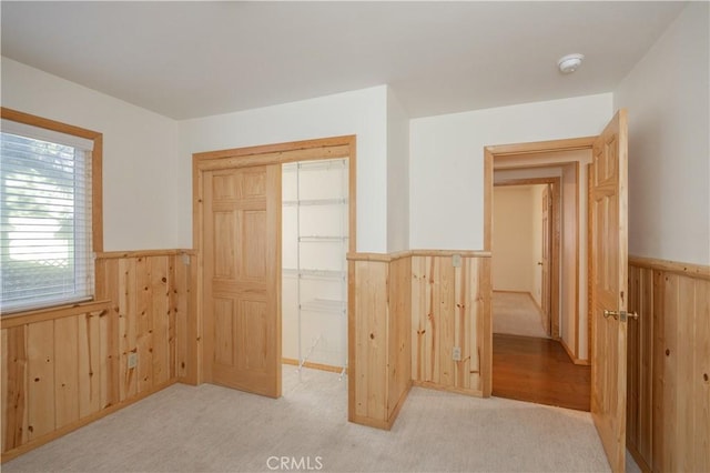 unfurnished bedroom with light carpet, wooden walls, and a closet