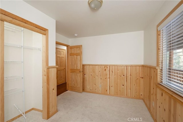 unfurnished bedroom featuring light colored carpet, wooden walls, and a closet