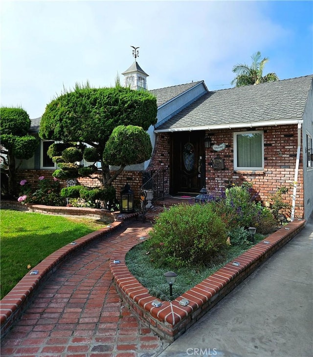 doorway to property with brick siding, a lawn, and a shingled roof