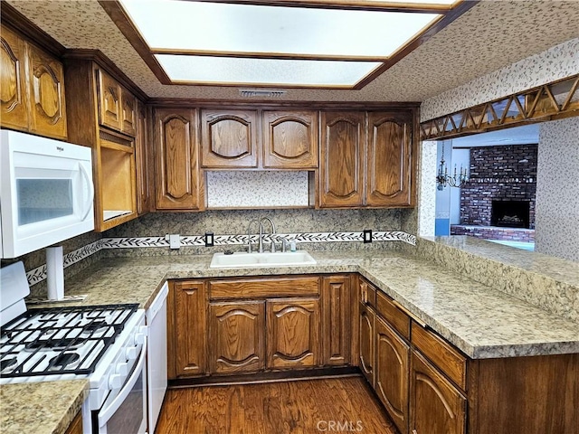 kitchen with white appliances, dark wood-style flooring, a peninsula, a sink, and backsplash