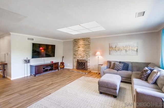 living room featuring ornamental molding, a stone fireplace, and light hardwood / wood-style floors