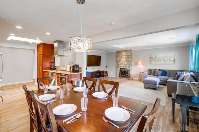 dining room with crown molding, a stone fireplace, light hardwood / wood-style floors, and a notable chandelier