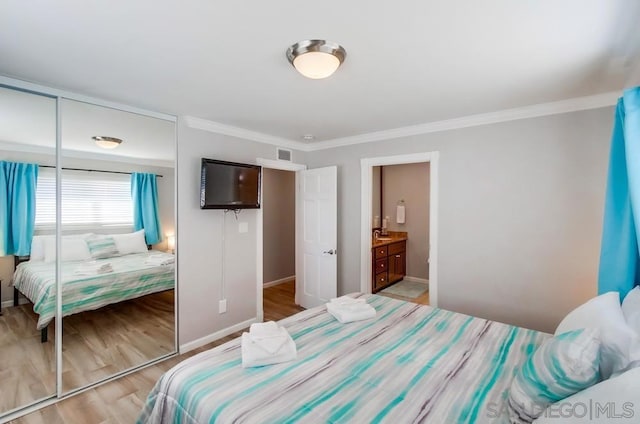 bedroom featuring ornamental molding, ensuite bathroom, light hardwood / wood-style floors, and a closet