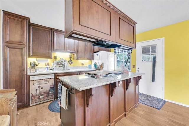 kitchen featuring sink, white appliances, a breakfast bar area, light hardwood / wood-style flooring, and light stone counters