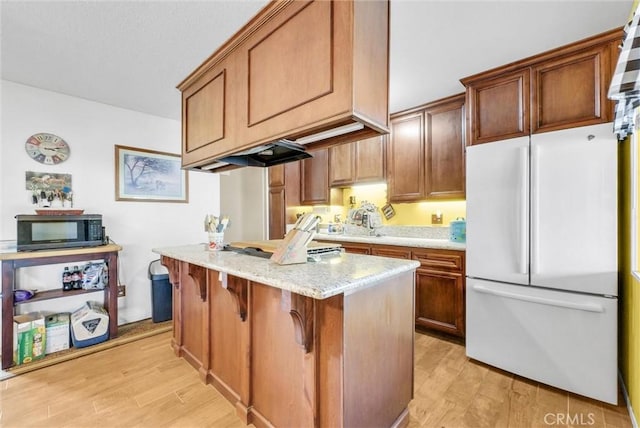 kitchen with light wood-type flooring, light stone countertops, a breakfast bar area, and white fridge