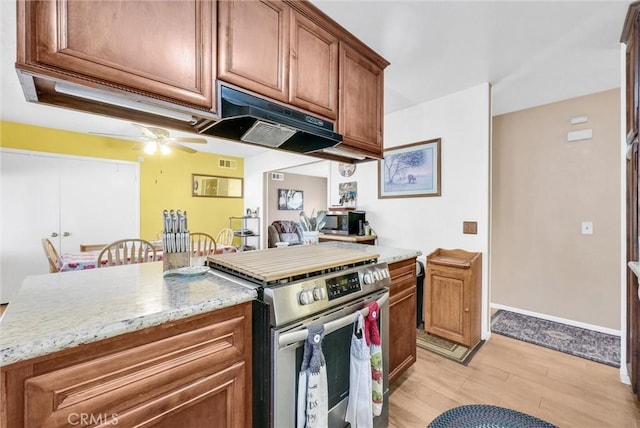 kitchen with light stone countertops, stainless steel range oven, ceiling fan, and light hardwood / wood-style flooring