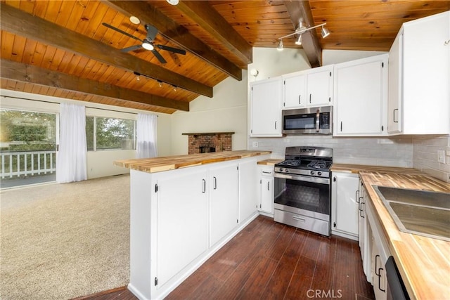 kitchen featuring ceiling fan, butcher block counters, lofted ceiling with beams, appliances with stainless steel finishes, and a peninsula