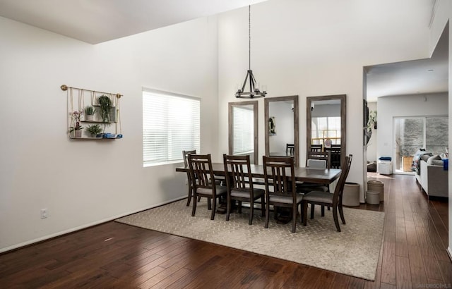 dining room featuring dark wood-type flooring, a towering ceiling, and a chandelier