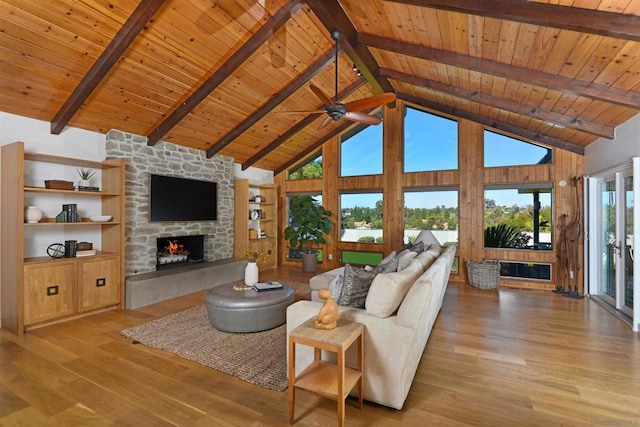 living room featuring a stone fireplace, high vaulted ceiling, wood ceiling, light hardwood / wood-style floors, and beam ceiling