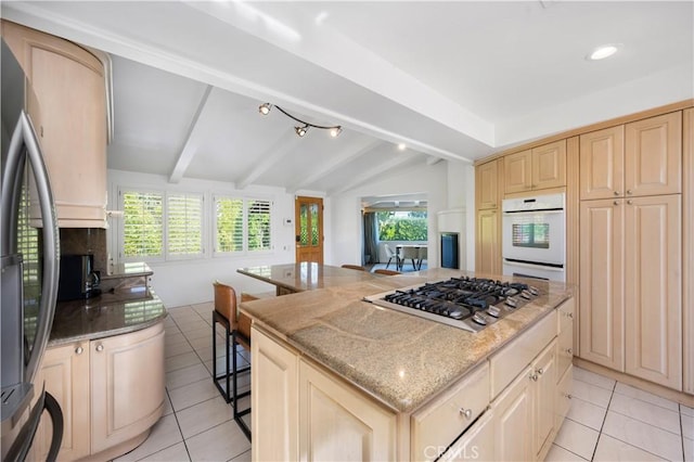 kitchen with a breakfast bar area, vaulted ceiling with beams, dark stone counters, a kitchen island, and stainless steel appliances