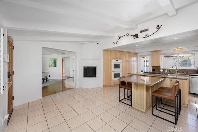 kitchen with a center island, appliances with stainless steel finishes, a kitchen breakfast bar, beam ceiling, and light stone countertops