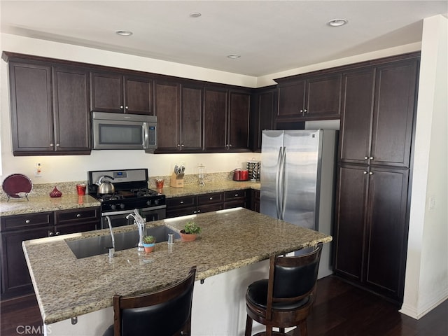 kitchen with appliances with stainless steel finishes, sink, light stone countertops, and an island with sink