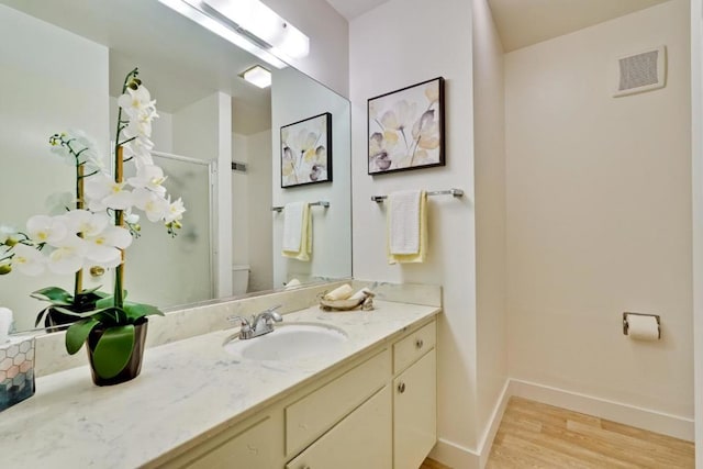 bathroom featuring wood-type flooring, toilet, a shower with shower door, and vanity