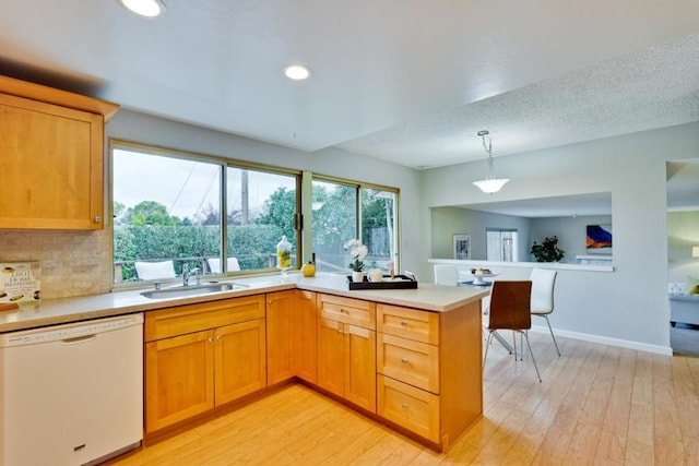 kitchen featuring sink, white dishwasher, decorative light fixtures, kitchen peninsula, and light wood-type flooring