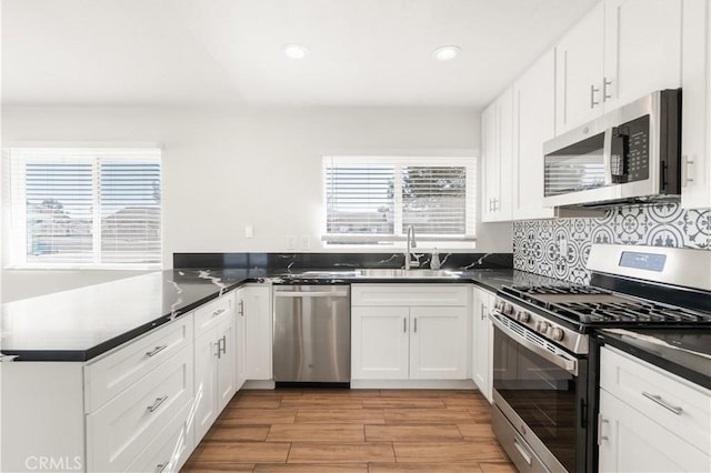 kitchen with appliances with stainless steel finishes, white cabinetry, sink, backsplash, and kitchen peninsula