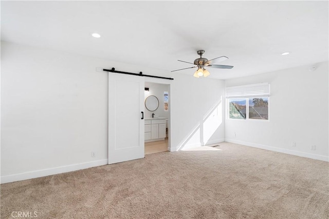 unfurnished room with a barn door, light colored carpet, and ceiling fan