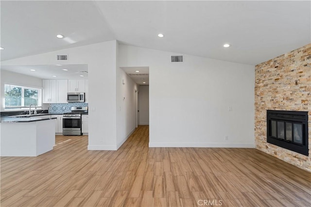 unfurnished living room with a fireplace, vaulted ceiling, sink, and light wood-type flooring