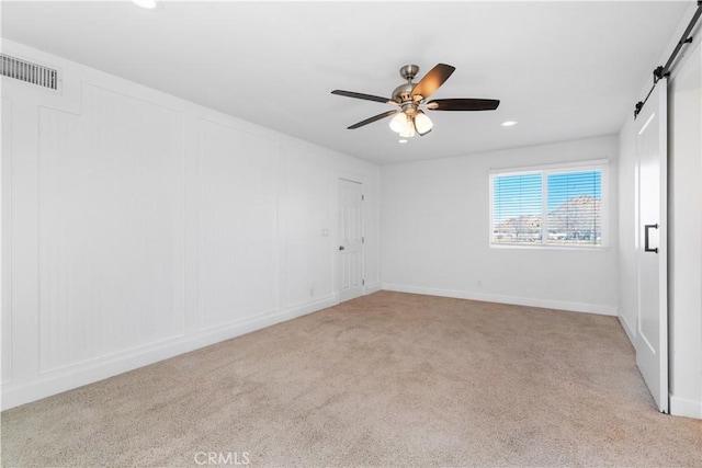 unfurnished room featuring light colored carpet, a barn door, and ceiling fan