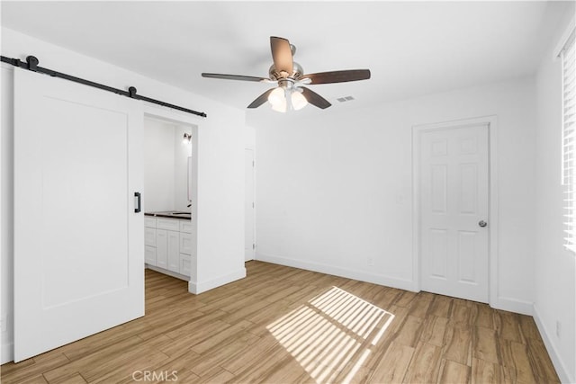 unfurnished bedroom with connected bathroom, light hardwood / wood-style floors, a barn door, and ceiling fan