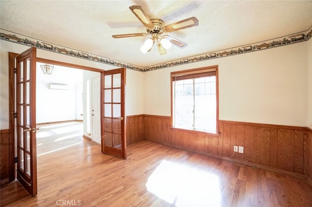 empty room with ceiling fan, wood walls, a textured ceiling, and light wood-type flooring